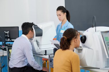 Cilinik hastaların görme yeteneğini test etmek için modern ekipman ayarlayan konsantre genç göz doktoru.