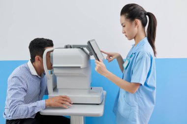 Genç bayan doktor, görme düzeltme ameliyatından önce hastanın gözlerini kontrol etmek için kırılma ölçer ayarlıyor.