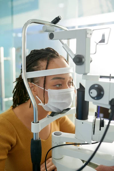 戴医疗面罩的年轻黑人妇女在诊所检查视力 — 图库照片
