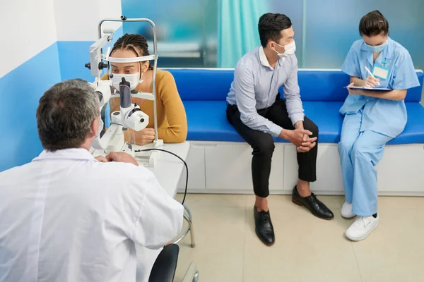 Pielęgniarka Medyczna Rozmawia Pacjentem Gdy Jego Żona Bada Oczy Autorefraktometrem — Zdjęcie stockowe