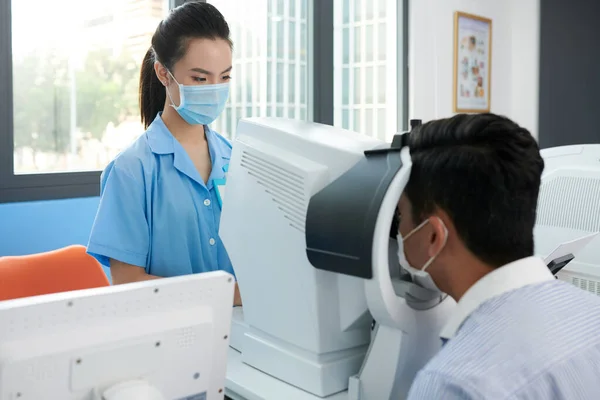 さまざまな病気の患者の目をチェックする医療用マスクの若い眼科看護師 — ストック写真