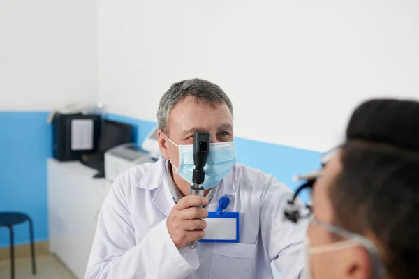 視力矯正手術前に患者を検査する際に網膜鏡検査ツールを使用する経験豊富な眼科医 — ストック写真