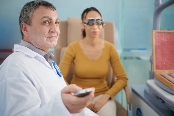 Smiling doctor pointing with laser pointer ophthalmology chart and asking patient to read letters on chart