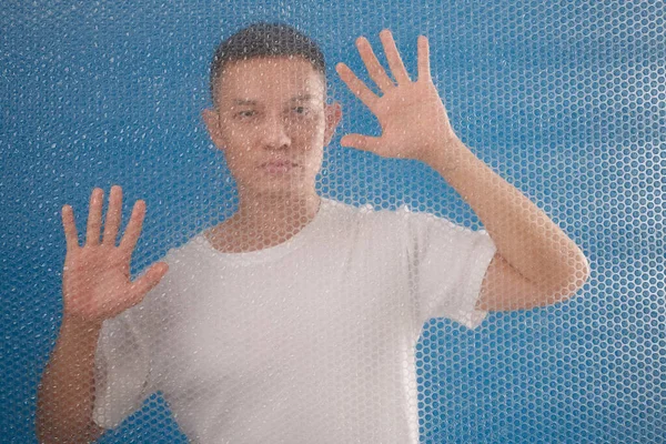 Portret Van Ernstige Jongeman Achter Plastic Bubble Wrap Tegen Blauwe — Stockfoto