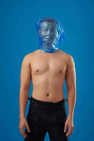 彼の頭の上に青いビニール袋で立っている深刻な恥知らずの若い男の肖像画 生態学の概念 — ストック写真