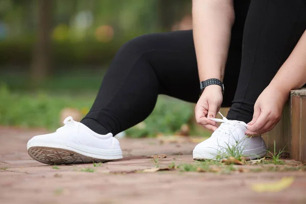 プラスサイズの若い女性の靴のレースを結ぶ午前中に公園で実行する — ストック写真