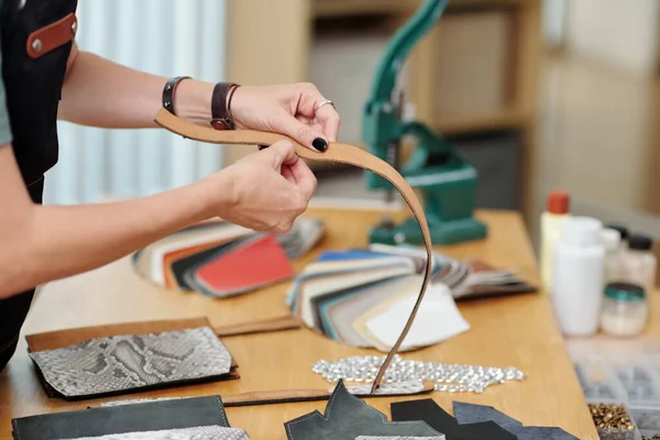 Hands of craftsperson working on leather belt for customer