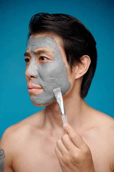 Man applying clay mask on face to clean pores