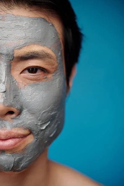 Half face of smiling man with clay beauty treatment on face looking at camera