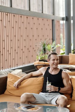 Spor salonunun dinlenme odasındaki kanepede dinlenen neşeli zinde adam.