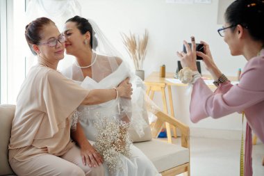 Bride kissing her mother of cheek when tailor photographing them for social media clipart