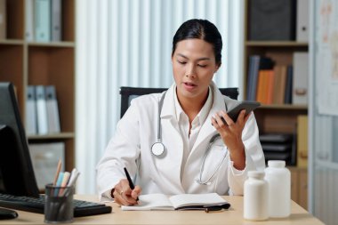 Doktor telefonda hastayla konuşuyor ve şikayetler yazıyor.