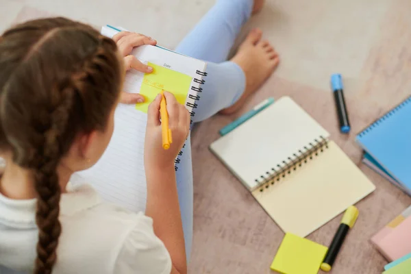 家庭での学校試験の準備の際に黄色のステッカーに関する重要な情報を書く女子高生 — ストック写真
