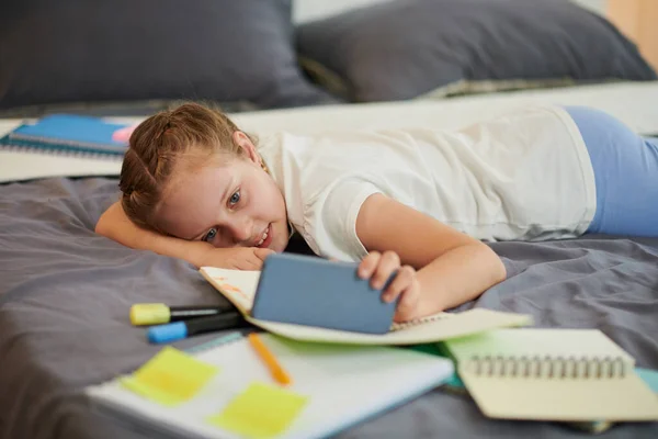 女孩在床上休息 做完作业后在智能手机上看娱乐节目 — 图库照片