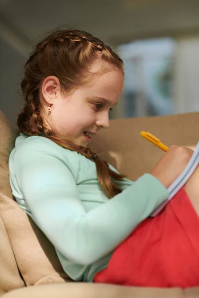 快乐的女孩坐在家里的沙发上 用记事本画画 — 图库照片