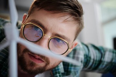 Gözlüklü adamın, rüzgar türbininin plastik modeline baktığı yakın plan görüntüsü.
