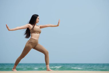 Sabahları kumlu sahilde yoga yapan genç bir kadın.