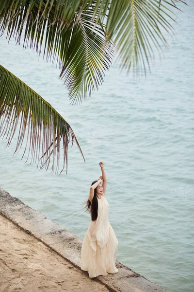 穿着米黄色长裙的年轻女子在海滨享受清风 — 图库照片