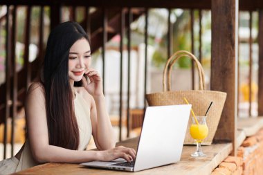 Plaj barında dizüstü bilgisayarda çalışan gülümseyen genç kadın.