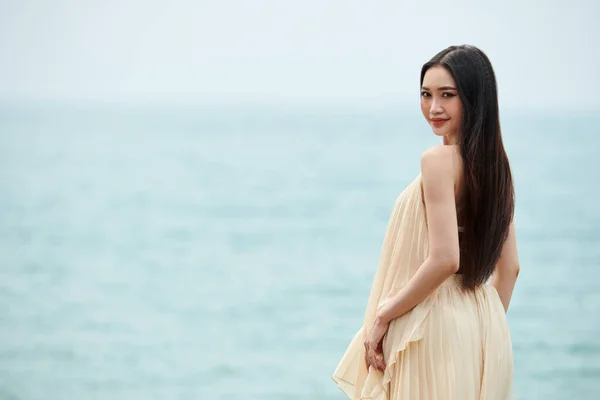 一位长发女子站在海滩上 转身对着镜头 — 图库照片