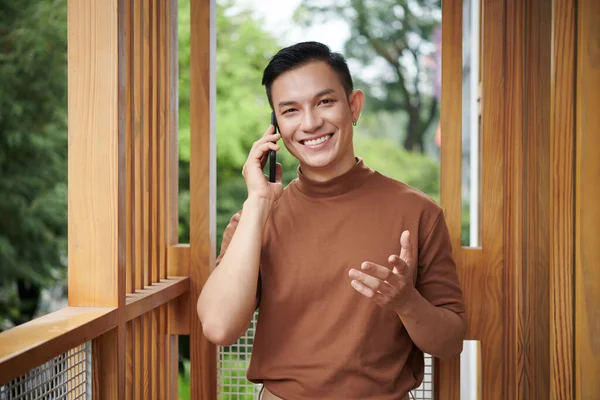 快乐自信的年轻人站在公寓阳台上给朋友打电话讨论最新消息的画像 — 图库照片