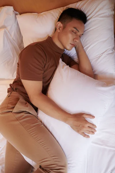 年轻男子睡觉时双腿中间有枕头 这使他的骨盆保持中立 并防止脊椎夜间旋转 — 图库照片