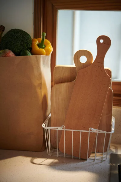 Basket with wooden cutting boards next to package of groceries on kitchen counter