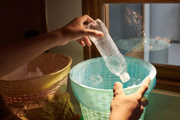 Young man sorting waste at home and putting plastic bottle in separate bin