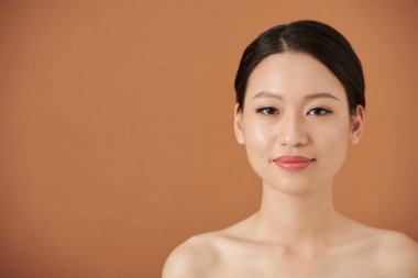 Kameraya bakarak eldivenli ve doğal makyajlı gülümseyen Vietnamlı genç bir kadının stüdyo portresi.