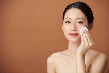 Gülümseyen genç kadın bodrum katındaki suya batırılmış pamukla makyajını yapıyor.