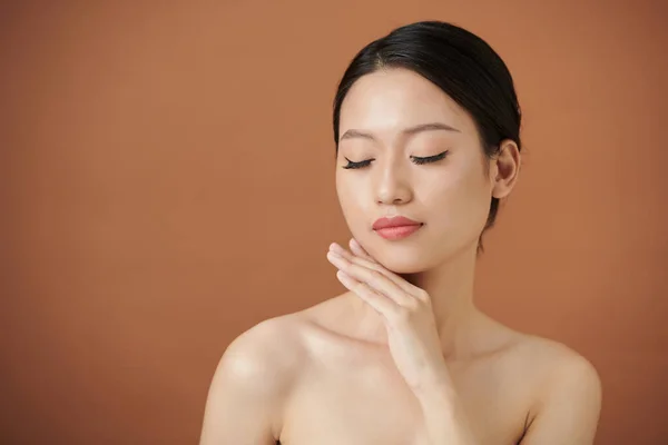 アジアの若い女性の肖像目を閉じて 彼女の柔らかい肌に触れる — ストック写真