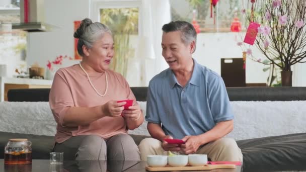 亚洲一对年长的夫妇坐在家里的沙发上 一边聊天 一边准备红包 准备在节日期间给孩子和家人寄钱 — 图库视频影像