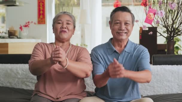 亚洲一对老年夫妇坐在装饰过农历新年的客厅里的沙发上 看着相机 手牵着手 微笑着说着祝福 — 图库视频影像