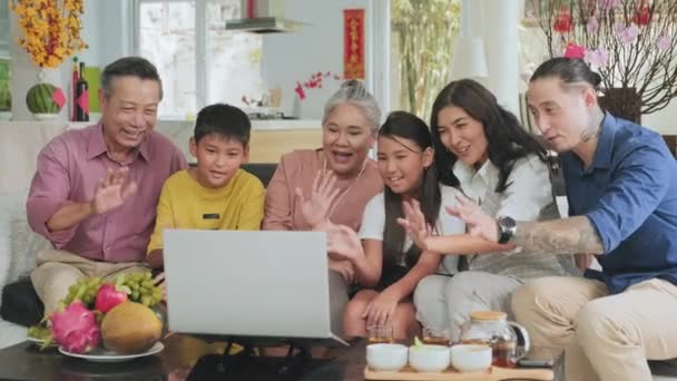 快乐的亚洲家庭坐在客厅的沙发上 一边一边在网上用笔记本电脑与亲戚们打招呼一边聊天 — 图库视频影像