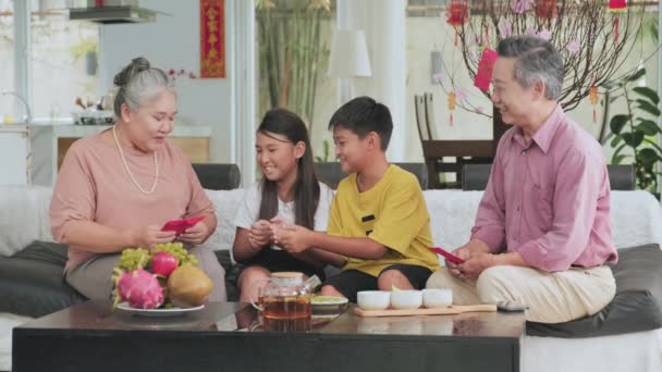 快乐的亚洲祖父母在家里共度佳节的同时 用红包送给客厅沙发上的孩子们一些幸运的钱 — 图库视频影像