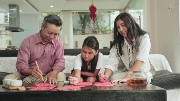 姉アジアの祖父 若い女性と娘はリビングでソファに座りながら書道を一緒に描き 家で家族の時間を過ごす — ストック動画