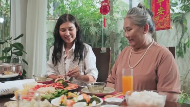陽気なアジアの女性は一緒に家でテトの休日の夕食を持っている間 祖母のためのプレート上にエビを置く — ストック動画
