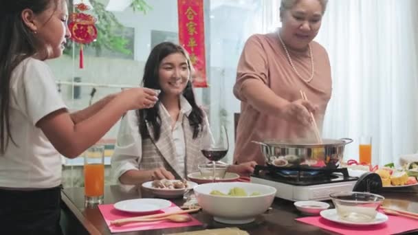 祖母は調理されたトウモロコシを提供しています小さな孫娘のための湯気鍋から家で家族の夕食を食べながらTetの休日 — ストック動画