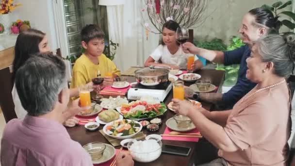 ホットポットと伝統的なベトナム料理とお祝いのディナーテーブルの周りに座っているアジアの家族の高角度ショット テトの家のお祝い中にトーストや飲酒でメガネをクリックしてください — ストック動画