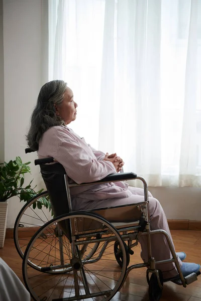 孤独なですシニア女性でパジャマで座っています車椅子で彼女のベッドルーム — ストック写真