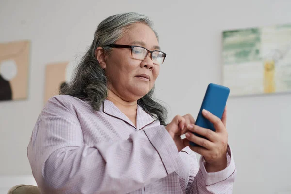スマートフォンのテキストメッセージに答える眼鏡の普及した高齢女性 — ストック写真