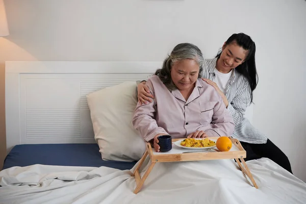 Caring Daughter Bringing Lunch Sick Senior Mother Sitting Her Bed — Stock Photo, Image