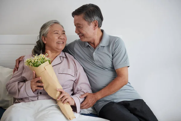 Счастливая Пожилая Женщина Смотрит Мужа Который Принес Букет Цветов Постель — стоковое фото