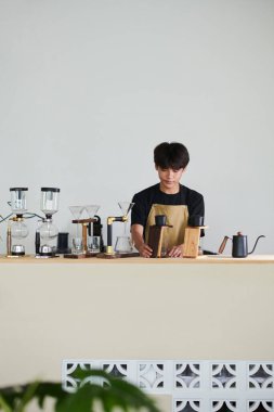 Kahvehanede çalışan dalgın genç adam kahve yaparken phin damlası filtresi kullanıyor.