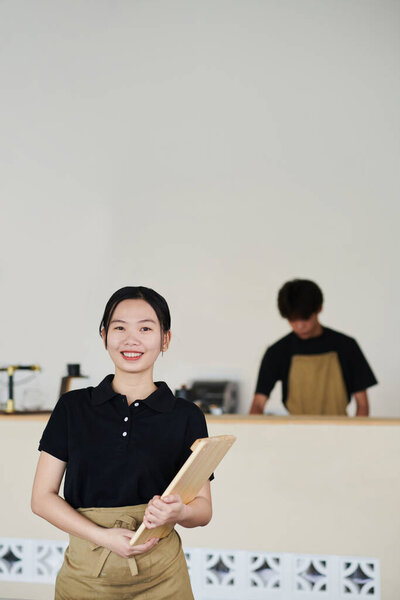Smiling young Vietnamese cafe waitress with serving wooden board