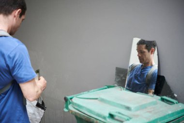 Sanatçının yansıması çöp konteynırındaki proje için kırık cam ve ayna parçaları topluyor.