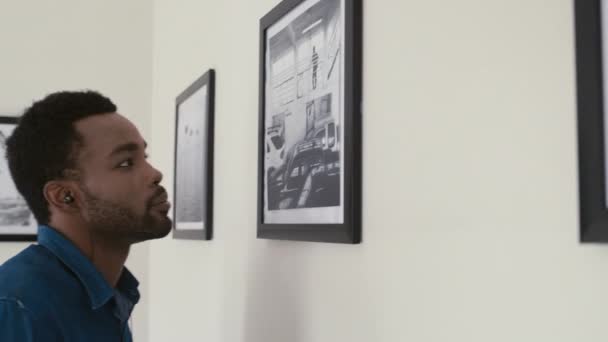 ギャラリーの展覧会を訪問しながら 若い黒人男性の音のガイドに耳を傾け 壁に写真を見てのショットを傾ける — ストック動画