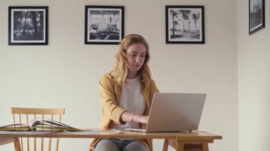 Sergi salonundaki masada oturan genç bayan galeri müdürü basılı resimleri kontrol ediyor ve dizüstü bilgisayarla çalışıyor.