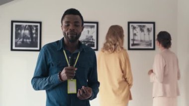Afrika kökenli Amerikalı TV muhabiri kameraya bakarken ve mikrofonla konuşurken sanat galerisindeki sergi hakkında haber yaparken belini kaldır.