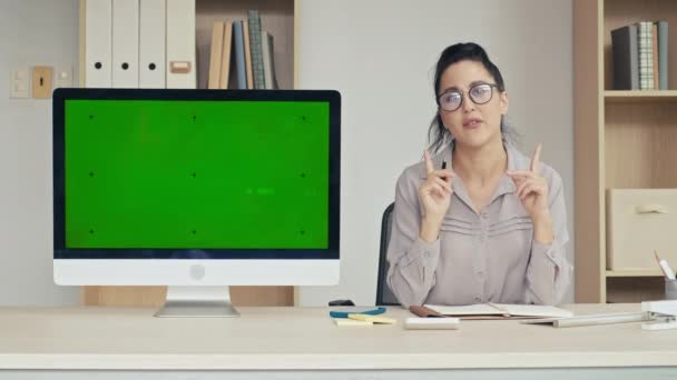 中等照度的女性看着相机 并在办公室用绿色彩色键屏在显示器上介绍应用情况 — 图库视频影像